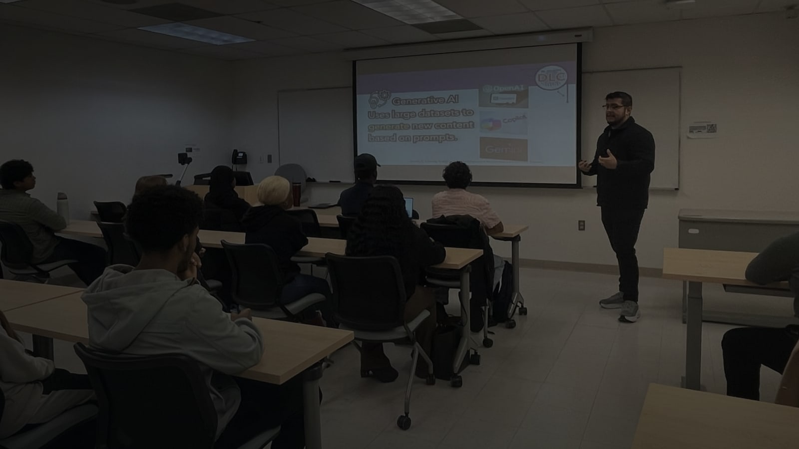 Daniel Umana standing at the front of a classroom, speaking to seated students, with a slide about generative AI on the screen behind him.