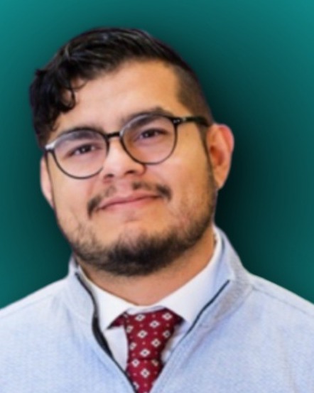 Daniel Umana, wearing glasses, a gray quarter zip and a red tie, against a teal studio backdrop.